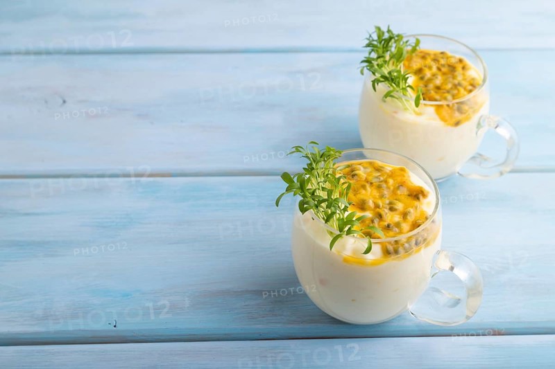 Mango yogurt with passionfruit and cilantro microgreen in glass on blue wooden background. Side view, copy space