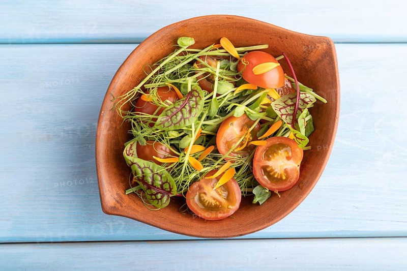 Vegetarian vegetables salad of tomatoes, marigold petals, microgreen sprouts on blue wooden background. Top view, flat lay, close up