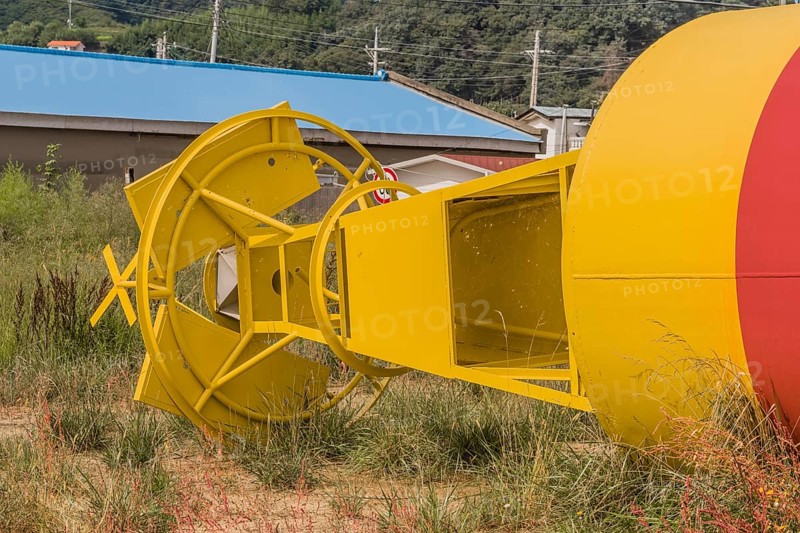 Bottom section of yellow and red ocean buoy laying in grass in fishing village