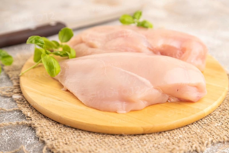 Raw chicken breast with herbs and spices on a wooden cutting board on a brown concrete background. Side view, close up, selective focus