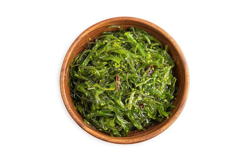 Chuka seaweed salad in brown wooden bowl isolated on white background. Top view, flat lay