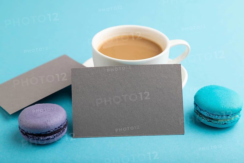 Gray paper business card mockup with blue and violet macaroons and cup of coffee on blue pastel background. Blank, side view, copy space, still life, close up. morning, breakfast concept