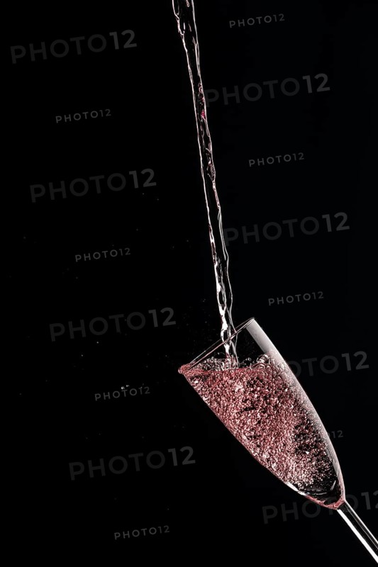 A champagne glass catches rose sparkling wine against a dark background