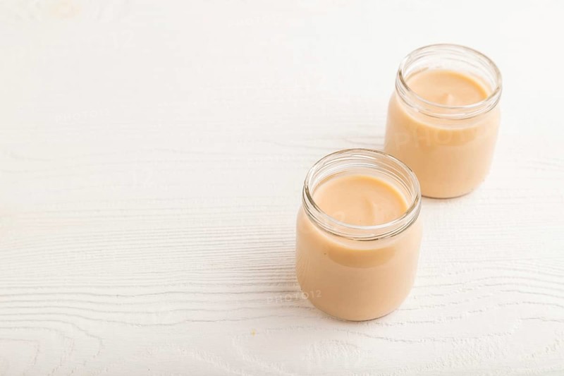 Baby puree with fruits mix, apple, banana infant formula in glass jar on white wooden background. Side view, copy space, artificial feeding concept
