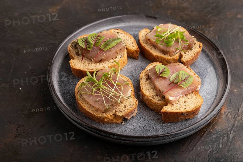 Bread sandwiches with jerky salted meat, sorrel and cilantro microgreen on black concrete background. side view, close up