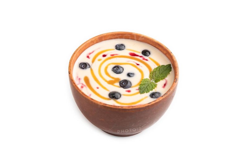 Yoghurt with bilberry and caramel in clay bowl isolated on white background. side view, close up
