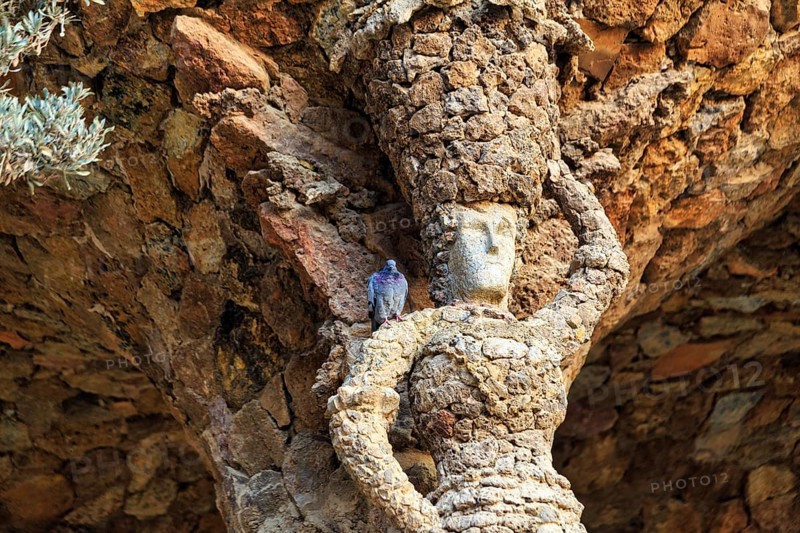 Dove sitting on the shoulder of a stone sculpture, Portico of the Washerwoman, colonnade in Park Güell, Barcelona, Spain, Europe