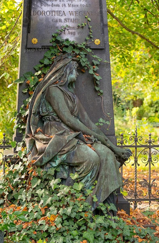 Detail of a green patinated cemetery sculpture surrounded by ivy and trees, autumn leaves, sculpture of a mourning woman with green patina in a cemetery in autumn, verdigris, gravestone with wrought iron fence, mourning, condolence, death, transience, cemeteries on Bergmannstraße, Berlin-Kreuzberg, Berlin, Germany, Europe