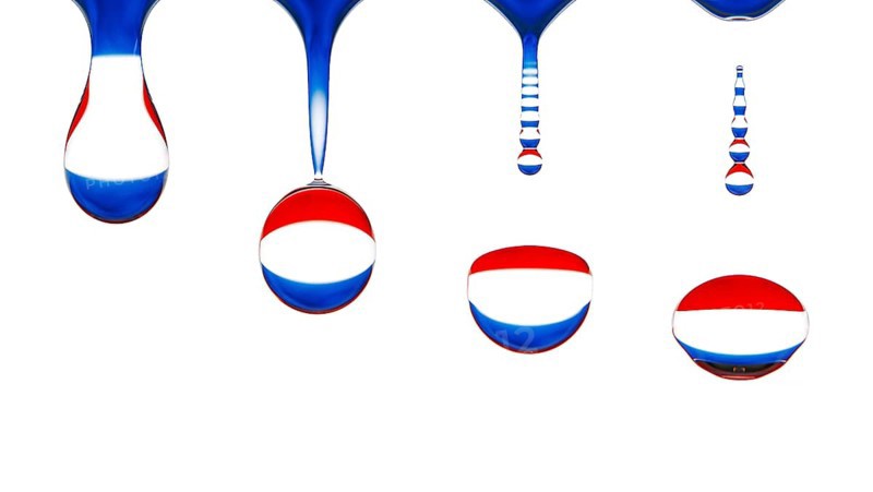 Macro shot of a drop of water dripping, the national flag of the netherlands is reflected in the drop