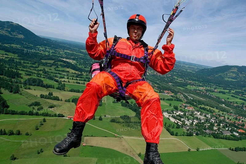 A man in signal red overalls hangs from a paraglider high above the meadows near Lenggries, pilot's perspective, Bavaria, Germany, Europe