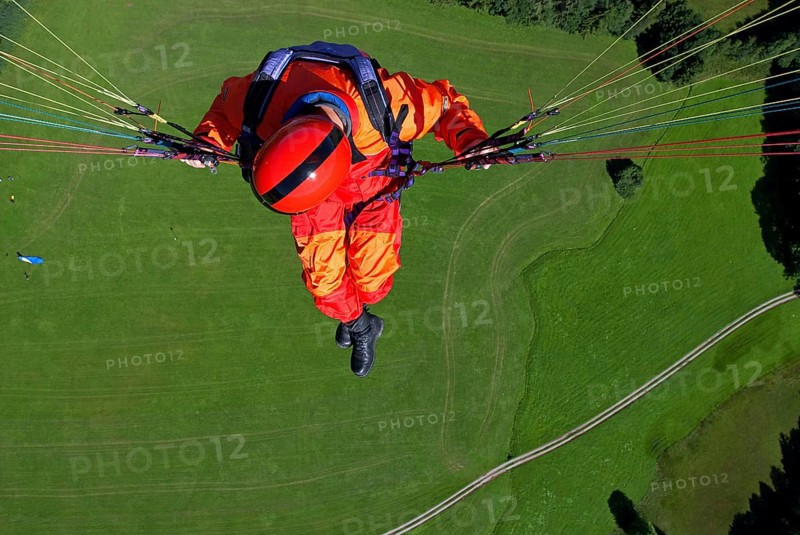 A man in signal red overalls hangs from a paraglider high above the meadows near Lenggries, pilot's perspective, Bavaria, Germany, Europe