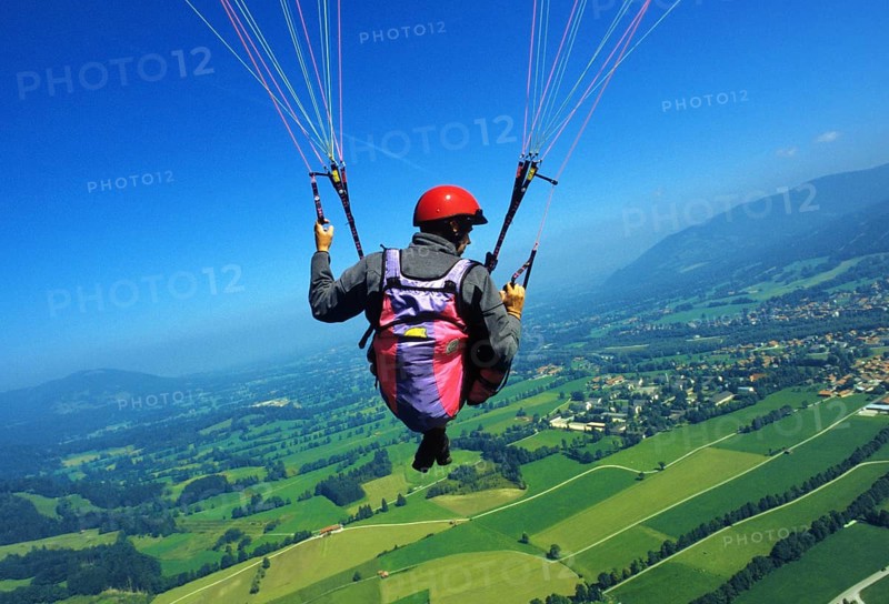 A man hangs from a paraglider high above the meadows near Lenggries, pilot's perspective, Bavaria, Germany, Europe