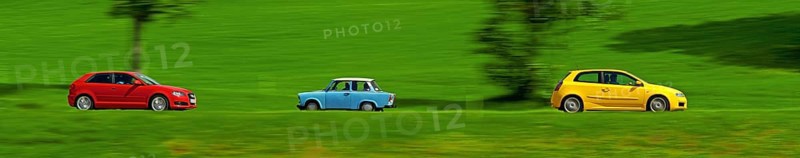 A red and a yellow car drive quickly through the green meadow landscape, a Trabant, also known as a Trabi, drives in the opposite direction