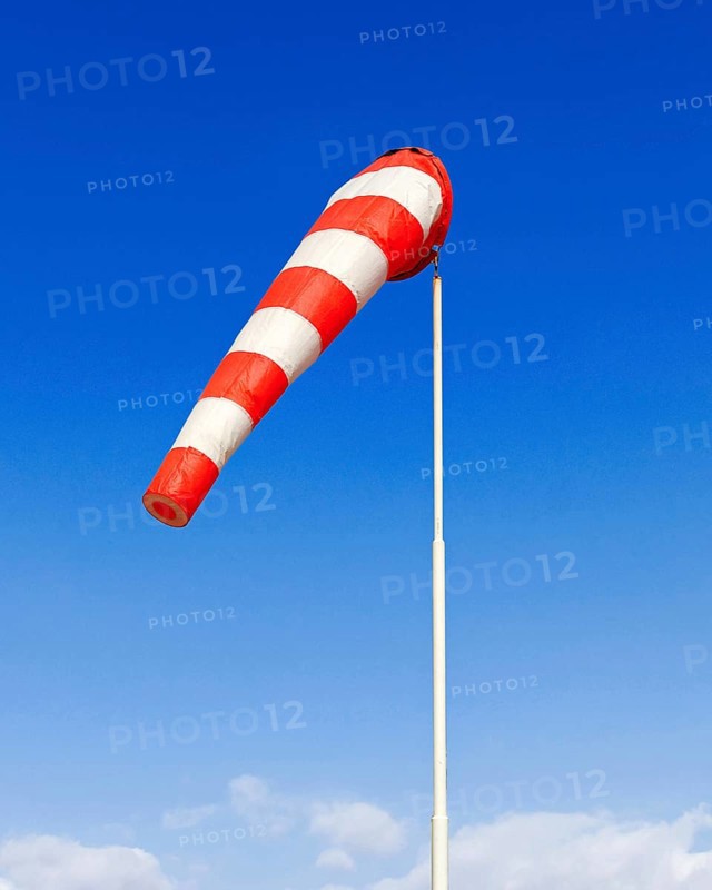 A red and white windsock blows in a light breeze against a blue sky