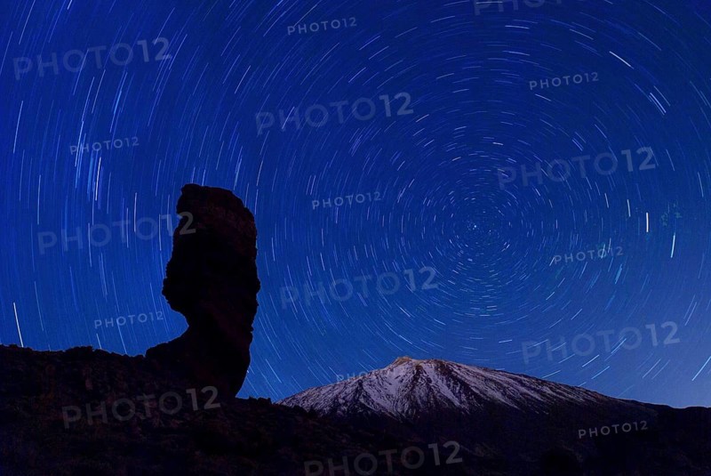 The Roque Cinchado at night with circling stars in the clear night sky and the summit of Pico de Teide, Tenerife, Canary Islands, Spain, Europe