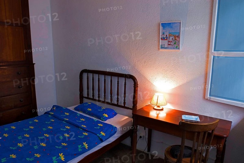 Bed and wooden table with illuminated bedside lamp in the room of a small, simple hotel or guesthouse in Santa Cruz de la Palma, La Palma, Canary Islands, Spain, Europe