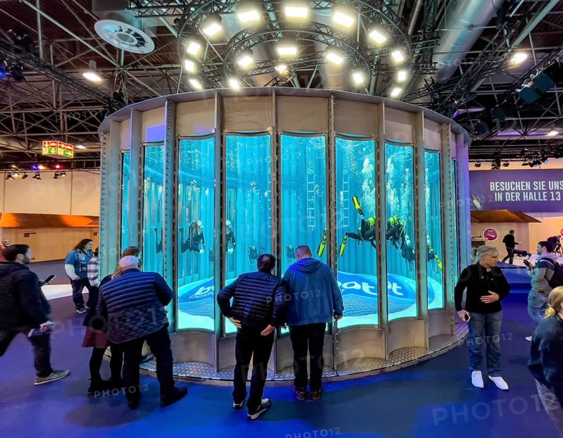 Full frontal view long shot of several divers in the water in a circular diving tower at the boot trade fair, boot Düsseldorf lettering on the ground, light installation above, trade fair visitors in front, Düsseldorf, North Rhine-Westphalia, Germany, Europe