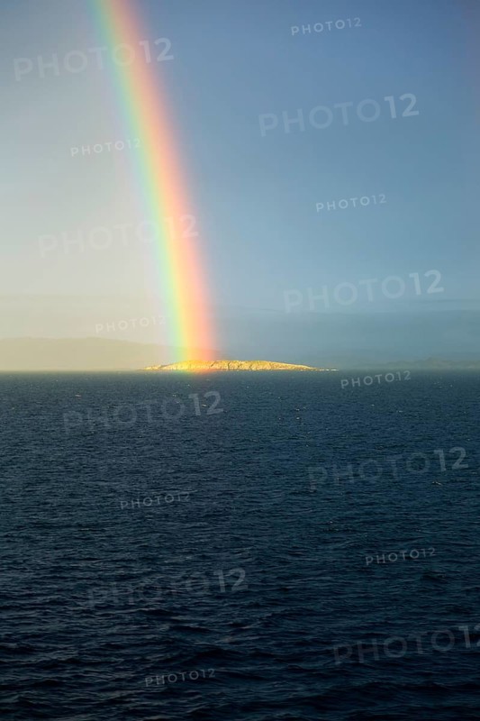 Seascape view of spectrum colours in rainbow over sea and island, Norway, Europe