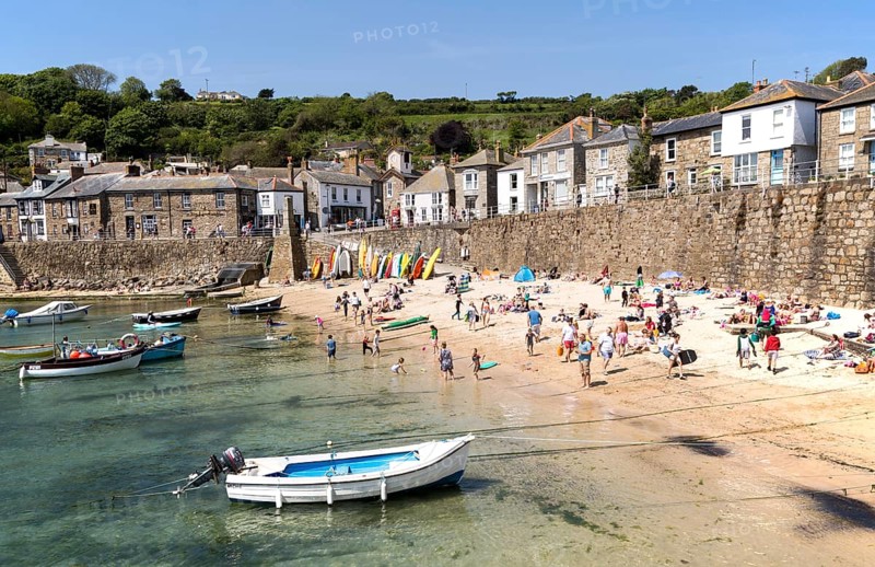 People on crowded beach in Mousehole village, Cornwall, England, UK