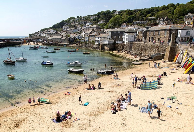 People on crowded beach in Mousehole village, Cornwall, England, UK
