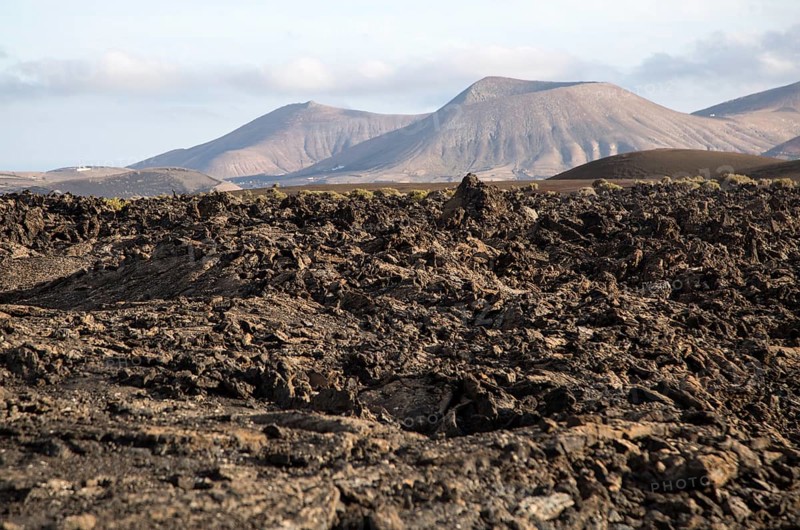 Volcanic landscape of solidified lava flows and distant cone volcanoes, near Yaiza, Lanzarote, Canary Islands, Spain, Europe