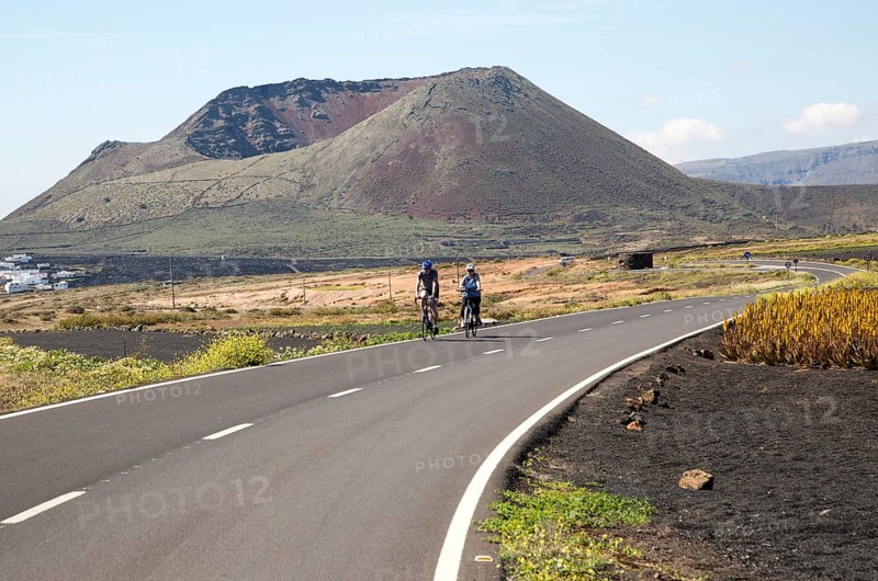 Cyclists on road leading to cone of Mount Corona volcano and Ye village, Haria, Lanzarote, Canary Islands, Spain, Europe
