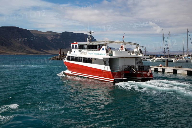 Tourist ferry boat Biosfera Express leaving the harbour Caleta de Sebo, La Isla Graciosa, with distant view of cliffs of Lanzarote, Canary Islands, Spain, Europe