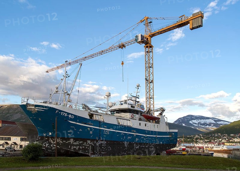 Construction crane towering above fishing boat boat in dry dock, Tromso, Norway, Europe