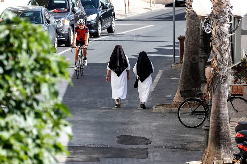 Two nuns walk across a street in Diana Marina, a man on a racing bike rides past, 28/05/2022