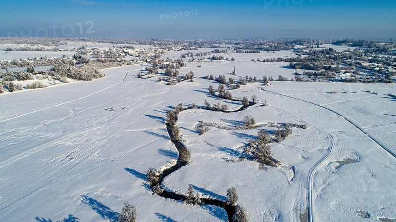 Drone shot of the river Schmutter meandering naturally through the snowy winter landscape of the Western Forests nature park Park near Augsburg, Swabia, Bavaria, Germany, Europe