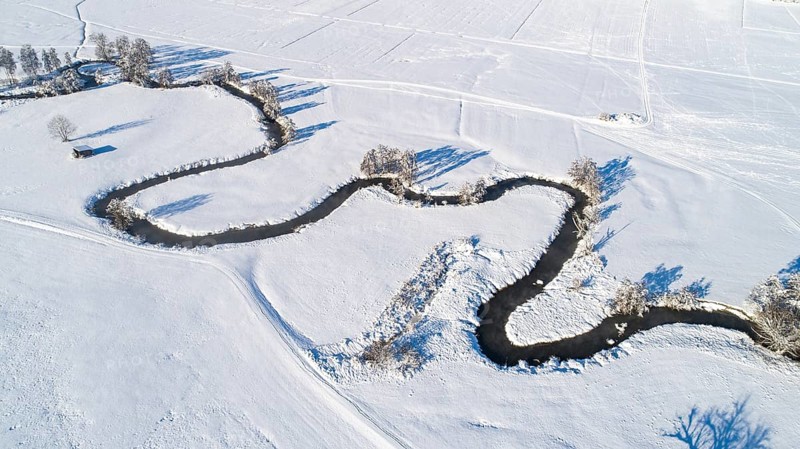 Drone shot of the river Schmutter meandering naturally through the snowy winter landscape of the Western Forests nature park Park near Augsburg, Swabia, Bavaria, Germany, Europe