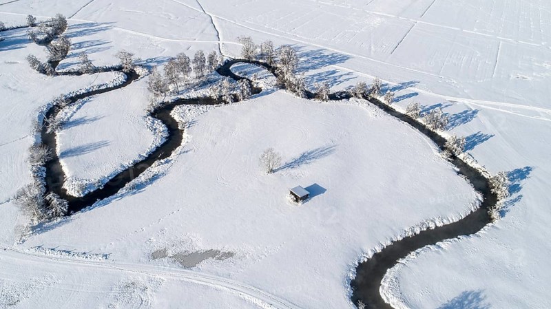 Drone shot of the river Schmutter meandering naturally through the snowy winter landscape of the Western Forests nature park Park near Augsburg, Swabia, Bavaria, Germany, Europe