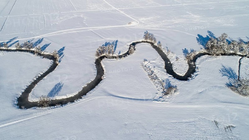 Drone shot of the river Schmutter meandering naturally through the snowy winter landscape of the Western Forests nature park Park near Augsburg, Swabia, Bavaria, Germany, Europe