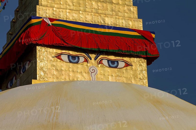 All-seeing eyes of Buddha, the Wisdom Eyes or Buddha's eyes, painted on the golden spire of Boudhanath, the Bouddha Stupa, the largest stupa in Nepal, Buddhist religious complex, UNESCO World Heritage Site and one of the Kathmandu Valley tourist attractions. Seen in the afternoon, on a clear, blue-sky, spring day, when the monument was lit by the setting sun. Photographed after the major reconstruction, that followed the 2015 earthquake, when the site was severely damaged. Kathmandu, Bagmati Province, Nepal, Asia