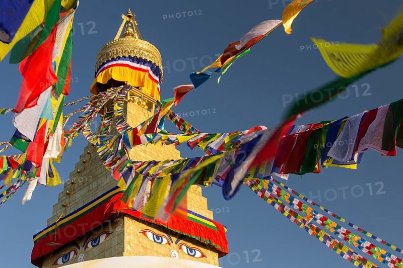 Golden spire of Boudhanath, the Bouddha Stupa, and colourful Buddhist prayer flags. It is the largest stupa in Nepal, important Buddhist religious complex, UNESCO World Heritage Site and a tourist attraction of the Kathmandu Valley. Seen late in the afternoon on a clear, blue-sky, spring day in the warm light of the setting sun. Photographed after the reconstruction, which followed the 2015 earthquake damages. Kathmandu, Bagmati Province, Nepal, Asia
