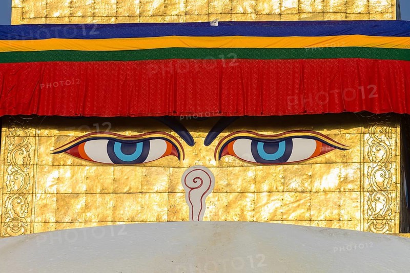 All-seeing eyes of Buddha, the Wisdom Eyes or Buddha's eyes, painted on the golden spire of Boudhanath, the Bouddha Stupa, the largest stupa in Nepal, Buddhist religious complex, UNESCO World Heritage Site and one of the Kathmandu Valley tourist attractions. Seen in the afternoon, on a clear, blue-sky, spring day, when the monument was lit by the setting sun. Photographed after the major reconstruction, that followed the 2015 earthquake, when the site was severely damaged. Kathmandu, Bagmati Province, Nepal, Asia