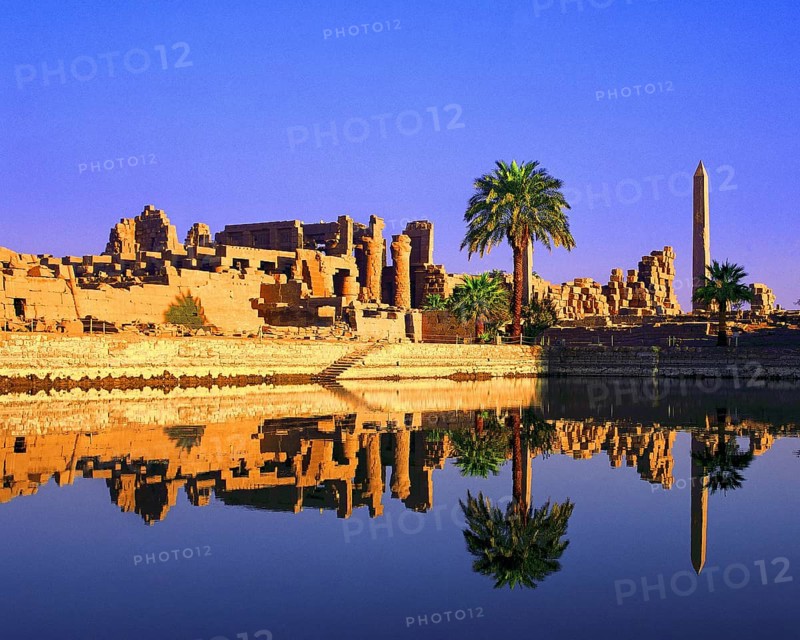 Palm trees grow beside the cistern, obelisk, columns and other remains at temple of Karnak, Luxor, Egypt, Africa