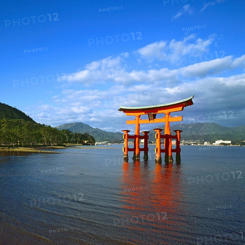 The bright red Sea-gate of Miyajima temple, Japan, against a background of sea and the low hills opf Miyajima island and the distant mainland of Japan, Asia
