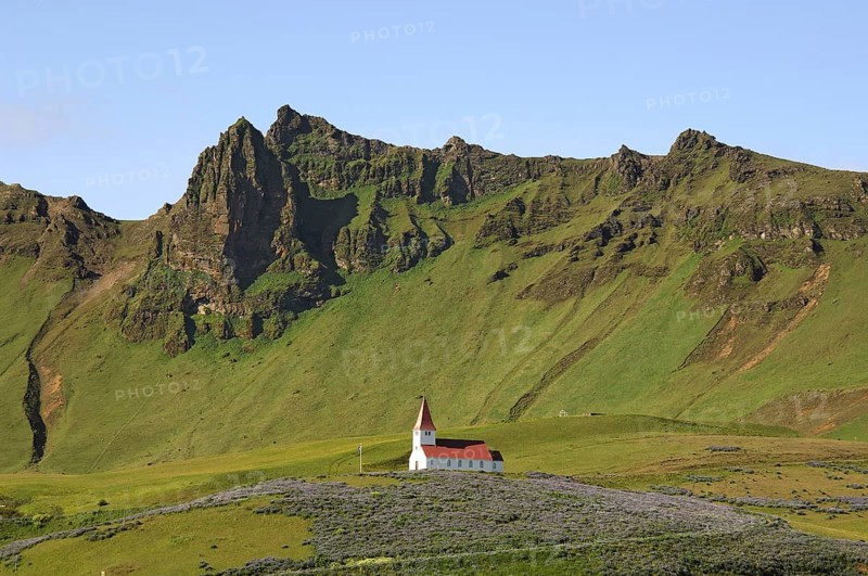 Small red and white church on a hilltop, surrounded by crags and steep hillsides, above the town of Vik, southern Iceland