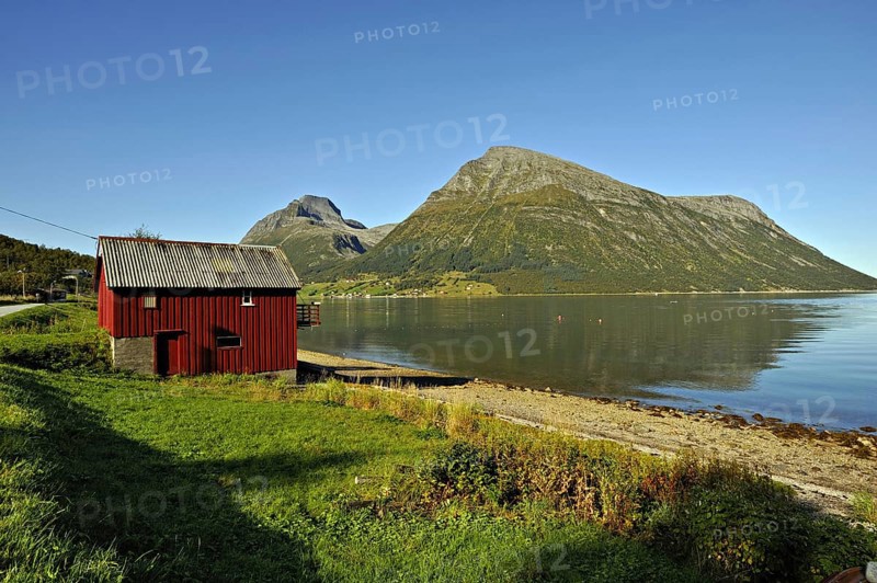 Red wooden boathouse at Lia with the island of Aldra and the Hjarttinden peaks behind, north-west Norway
