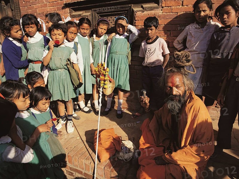 A group of young schoolgirls gathers round fascinated by a Hindu holy man or saddhu outside the former Royal Palace in Patan in the Kathmandu valley, Nepal, Asia