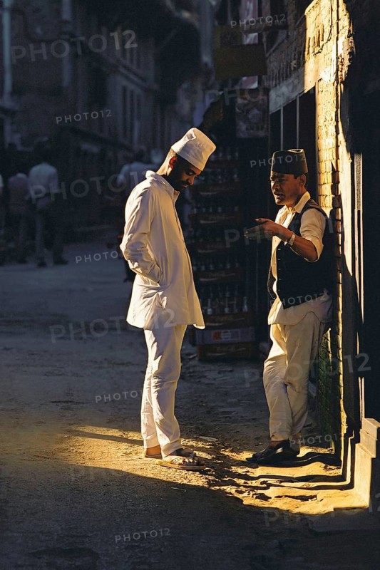 Two men chat in a patch of sunlight in a Kathmandu backstreet, Kathmandu, Nepal, Asia