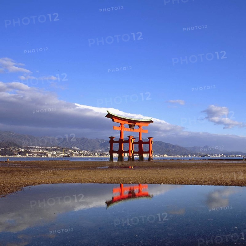 The bright red Sea-gate of Miyajima temple, Japan, against a background of sea and the low hills opf Miyajima island and the distant mainland of Japan, Asia