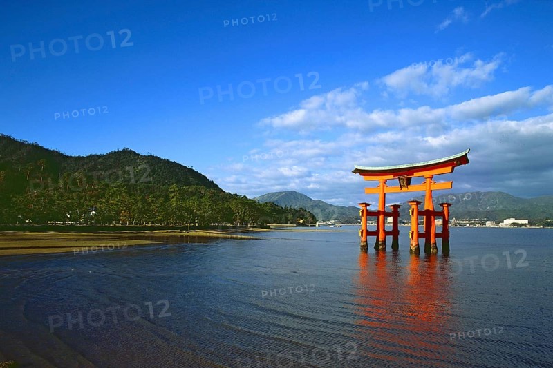The bright red Sea-gate of Miyajima temple, Japan, against a background of sea and the low hills opf Miyajima island and the distant mainland of Japan, Asia
