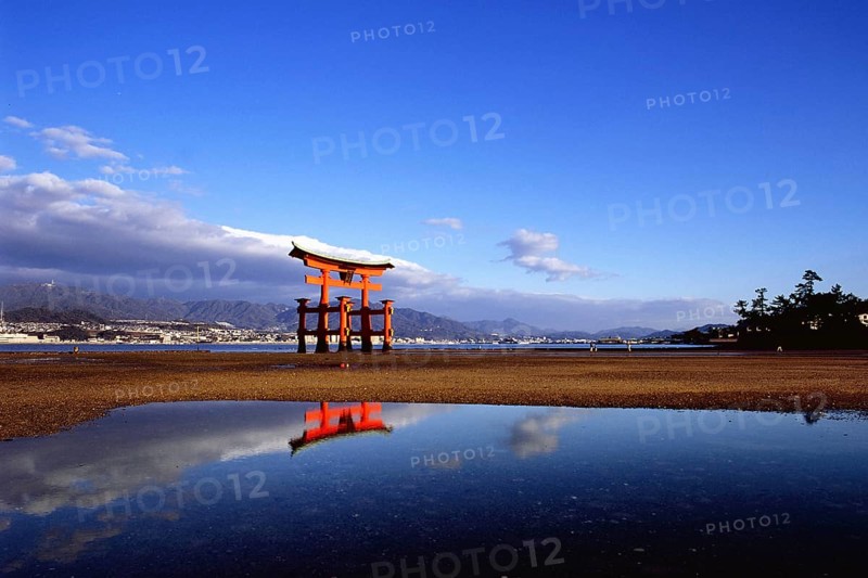 The bright red Sea-gate of Miyajima temple, Japan, against a background of sea and the low hills opf Miyajima island and the distant mainland of Japan, Asia