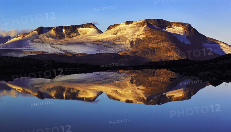 Early-morning light on the Fannaraken peaks with a mirror-like reflection in a glacial lake, Jotunheim region, Norway, Europe