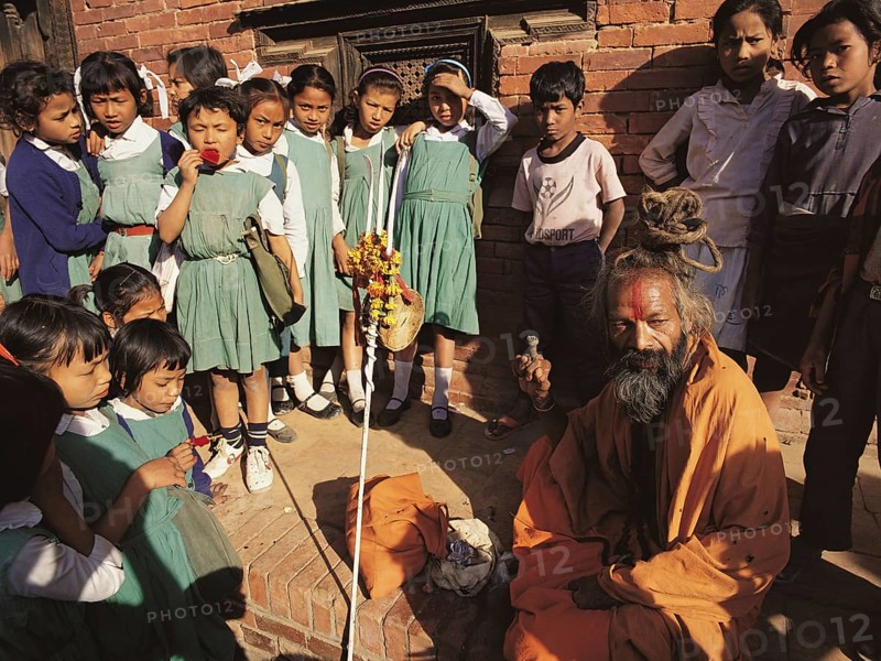 A group of young schoolgirls gathers round fascinated by a Hindu holy man or saddhu outside the former Royal Palace in Patan in the Kathmandu valley, Nepal, Asia