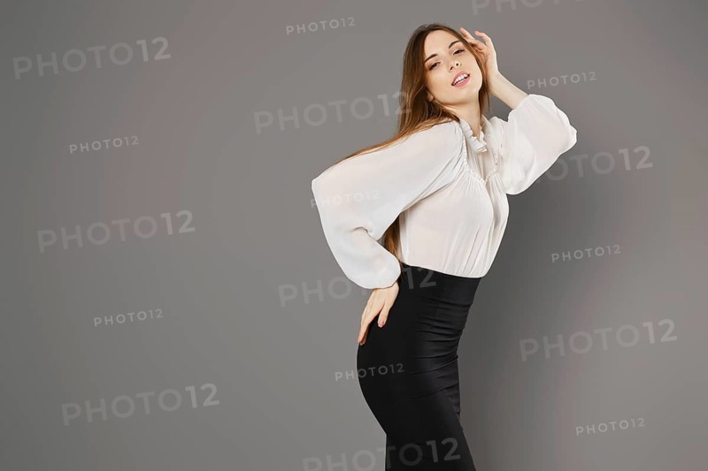Gorgeous young woman in pencil skirt and blouse posing in grey studio