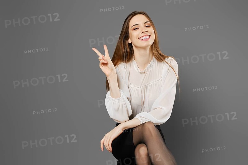 Satisfied young woman sitting on a chair raising two fingers showing a symbol of victory
