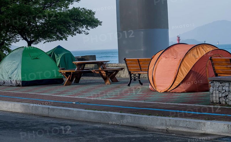 Tents set up on walkway next to picnic table and benches with the ocean and a bridge support column in the background in South Korea